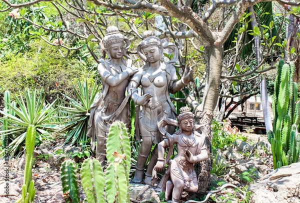 Fototapeta Ancient statues in lush tropical garden with cacti and trees under vibrant sunny atmosphere
