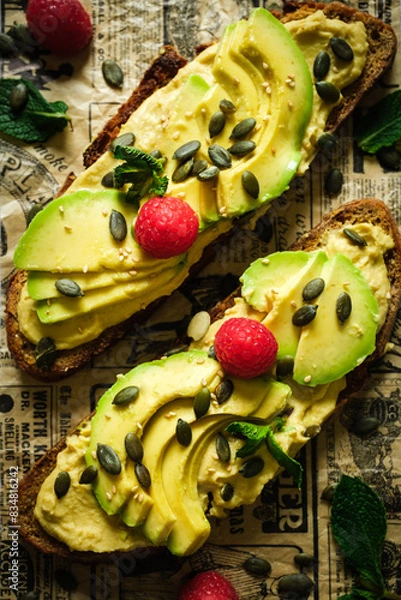 Obraz Detail of two toasts of bread with avocado, decorated with pumpkin seeds, mint and raspberry. Urban food.