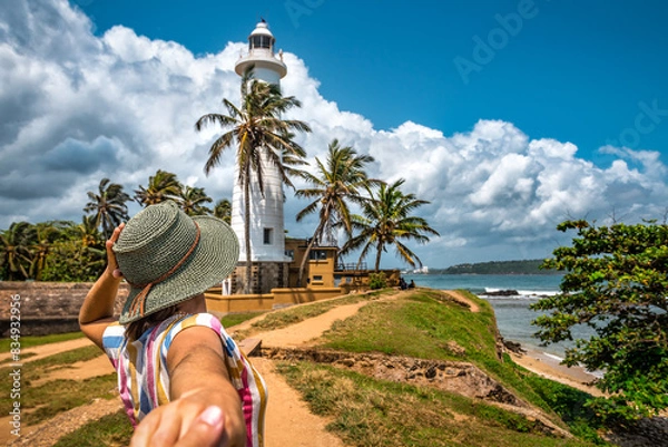 Obraz Tourist woman in hat holds man hand an going to the lighthouse on tropical island. Fort Galle. Sri Lanka