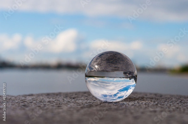 Obraz Glass transparent ball on river background and grainy surface