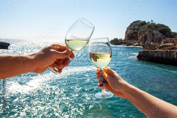 Obraz Two hands, male and female, hold glasses of champagne against the backdrop of the sea and mountains. Vacation, travel concept