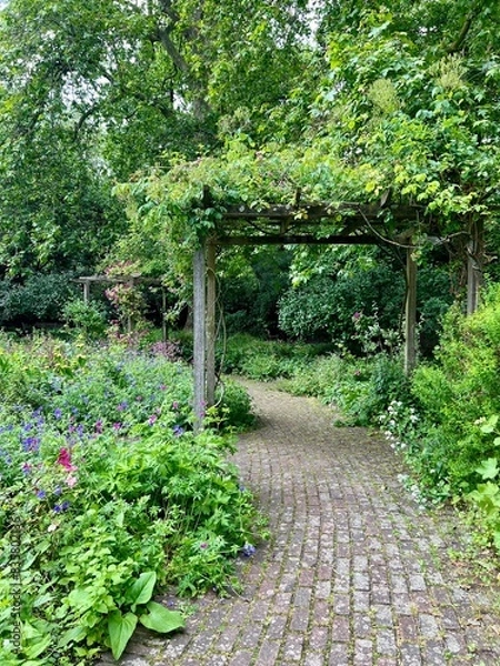 Obraz An English Garden with a pergola and lush spring flowers, grass and a cobblestone pathway.  Taken during the day, no people.