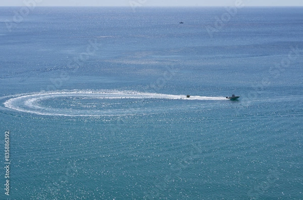 Fototapeta The boat rides tourists on tubing and completes a loop turn on the sea surface (Rhodes, Greece)