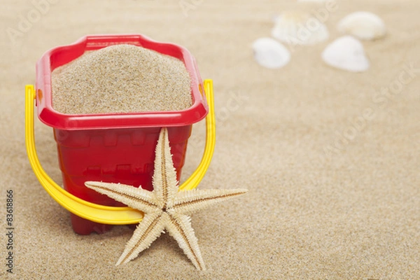Fototapeta A starfish and plastic bucket at the beach 