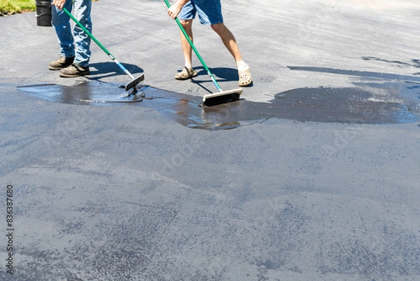Obraz Two men applying sealer on asphalt driveway with brush and squeegee on sunny day