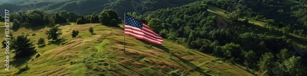 Fototapeta An aerial view of a large United States flag displayed on a hillside, surrounded by lush green trees and open sky.