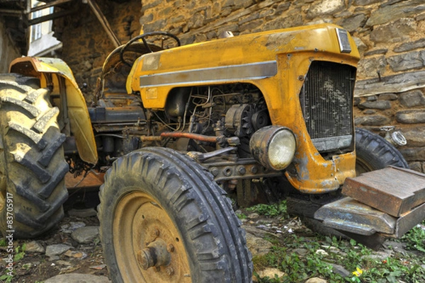 Fototapeta old tractor in front of the stone wall