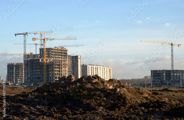 Fototapeta Tower cranes constructing a new residential build. Pouring concrete into formwork of building at construction site. Laying or replacement of underground storm sewer pipes. Concrete drainage pipe.