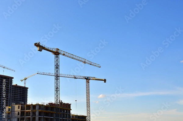 Fototapeta Tower cranes working at construction site on blue sky background. Construction process of the new modern residential buildings