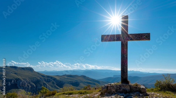 Fototapeta A Christian cross on a high plateau during a clear day, with the unobstructed sun illuminating the cross and the bright blue sky providing a vivid canvas behind it.