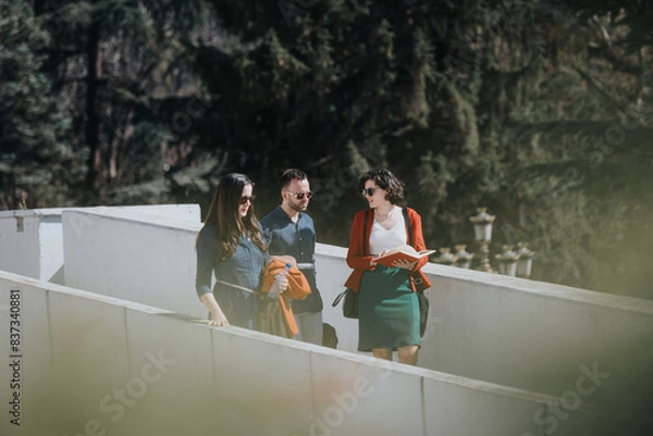 Fototapeta Three business professionals engaged in a discussion while walking outdoors, with a document in hand and casual expressions.