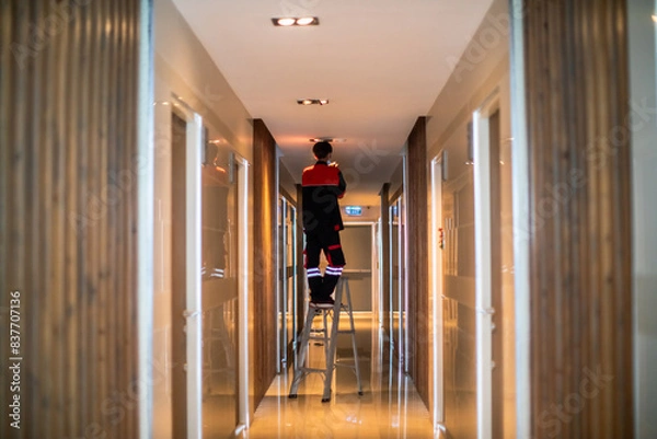 Fototapeta Technician is replacing or repair a smoke detector in an office building or condominium.  Technician is checking a fire alarm system at smoke detector.