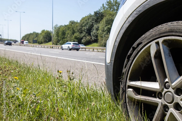 Fototapeta A car with a flat tyre after a large blow out on the highway showing a large slit in the tyre at the side of the M25 motorway in London in the UK