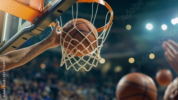 Fototapeta A basketball falls through a hoop during a game, capturing the moment of scoring in a brightly lit gym