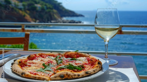 Fototapeta Pizza and a glass of wine are on a table in a cafe against the backdrop of the sea