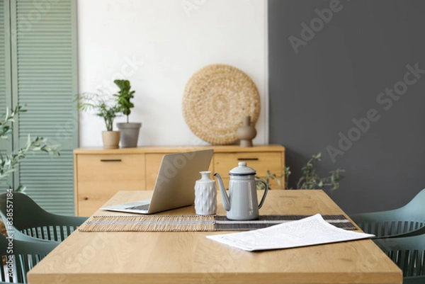 Fototapeta laptop with teapot and newspaper on dining table in room