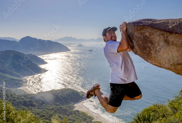 Obraz Adventurous climber hangs off Pedra do Telégrafo with breathtaking coastal view in Rio de Janeiro
