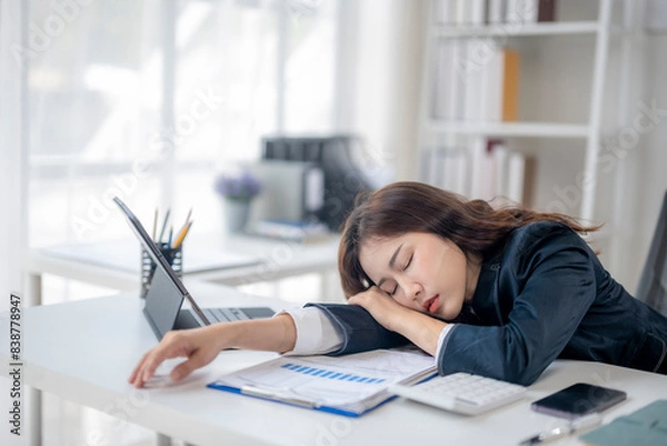 Fototapeta A woman is sleeping on her desk with a laptop and a stack of papers