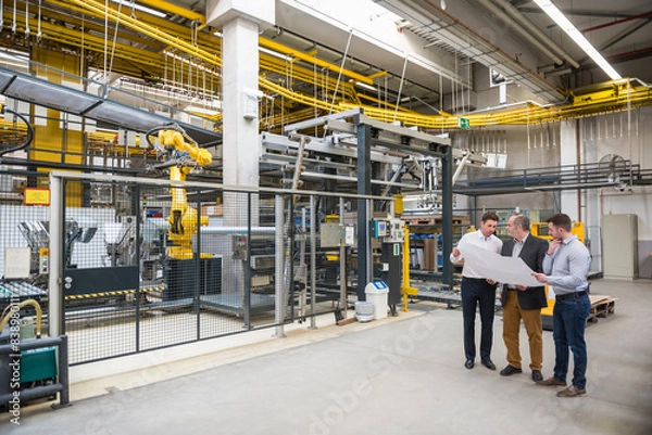 Fototapeta Three men with blueprint talking in factory shop floor