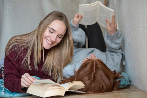 Fototapeta Two friends lying side by side on the floor reading books