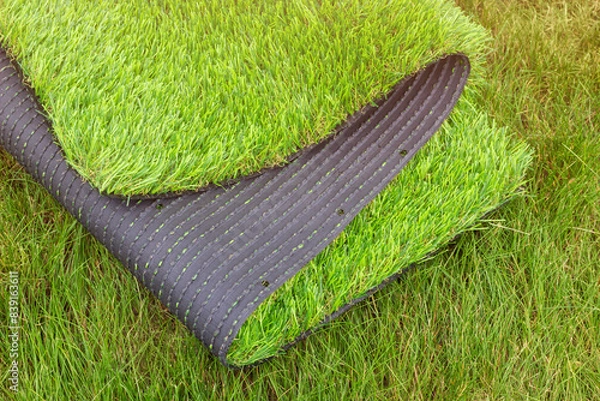 Fototapeta The roll of synthetic grassyard surface for gardening. Decorative lawn cover with vibrant green color. The difference between the natural and artificial grass.