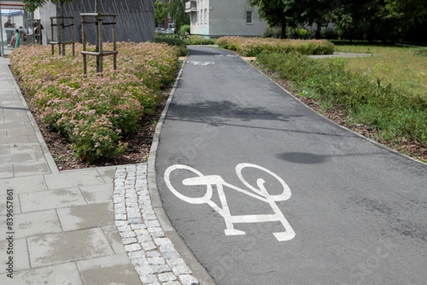 Fototapeta Bicycle path with markings in a summer city. "Bicycle" sign on the sidewalk.