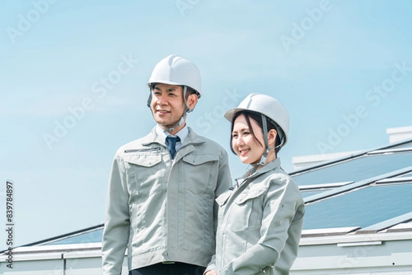 Fototapeta 太陽光発電・ソーラーパネルの前に立つ電力会社・電気工事業者の作業着姿の技術者・ビジネスパーソン
