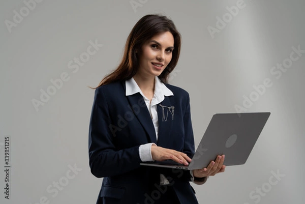 Fototapeta A woman in a suit is holding a laptop computer