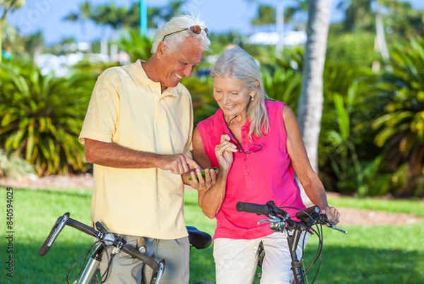 Fototapeta Happy Senior Couple on Bicycles In a Park Using a Smartphone