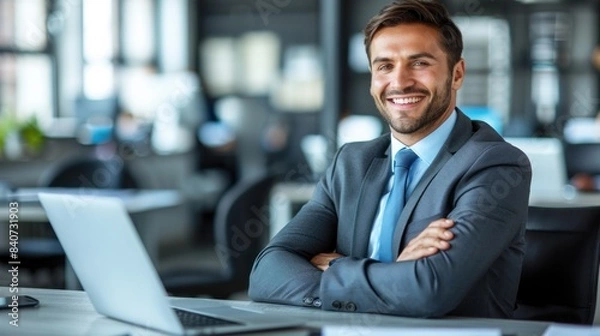 Obraz A businessman sits at his desk with a laptop open in front of him, smiling confidently at the camera