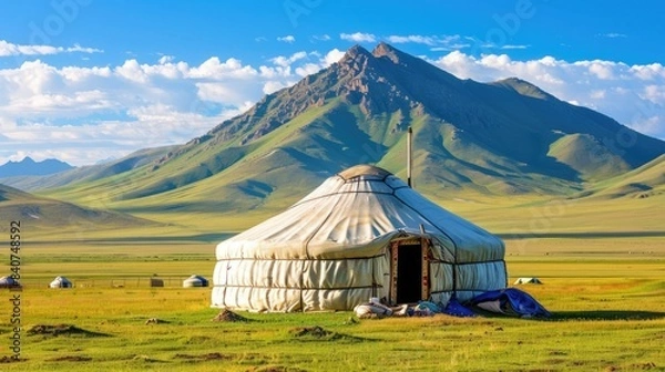Fototapeta a yurt in the grassland, on a green meadow with a blue sky and white clouds. A traditional Kazakh yurt building among mountains and forest.