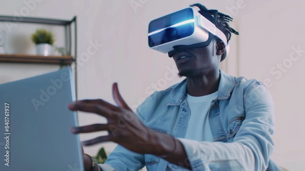 Fototapeta Man immersed in virtual reality, wearing a headset and interacting with a laptop, in a minimalistic, well-lit room.