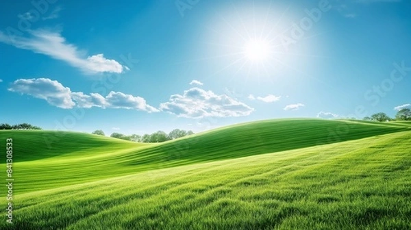 Fototapeta Lush green rolling hills under a clear blue sky with sunlight and scattered white clouds on a bright summer day in a tranquil countryside landscape