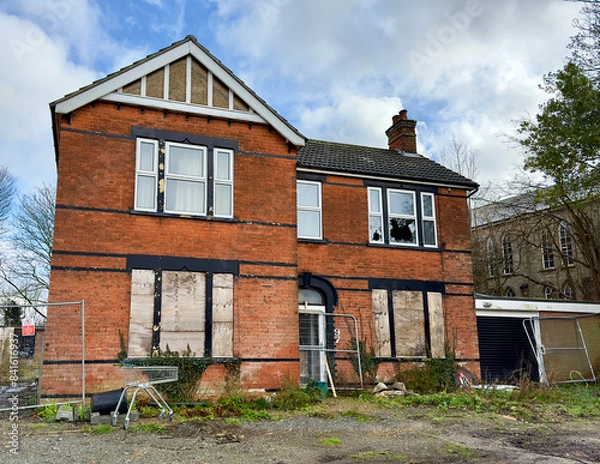 Fototapeta A derelict detached house with boarded up windows downstairs and a broken window upstairs. 