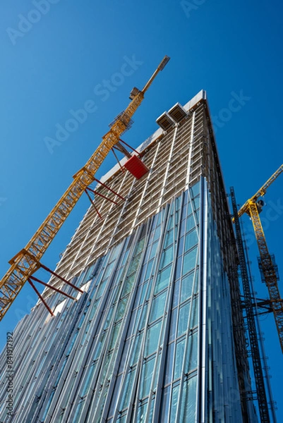 Fototapeta Looking up to a high-rise building on a Construction Site with a yellow crane