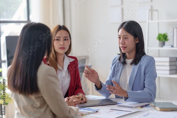 Fototapeta Three businesswomen having a meeting in a modern office, discussing important matters with determination and collaboration.