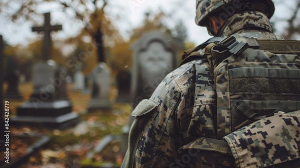 Fototapeta A soldier in military uniform wearing a helmet at a military cemetery. A veteran's shoulder against the background of graves.
