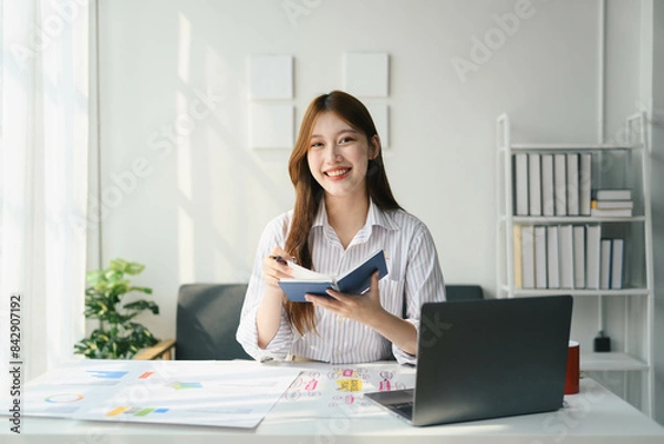 Fototapeta Student woman is sitting at a desk with a laptop and a notebook