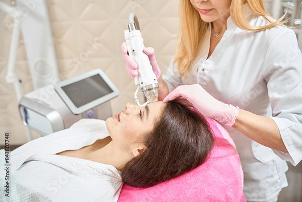Fototapeta Client undergoing radio frequency microneedling treatment by cosmetologist