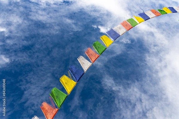 Fototapeta Colorful Tibetan prayer flags attached to a string flying in air against blue sky with clouds   