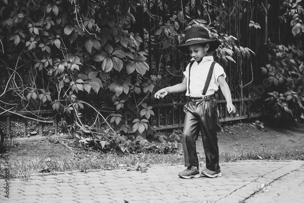 Fototapeta an afro boy dressed in the style of the 20s walks down the street looking at his feet