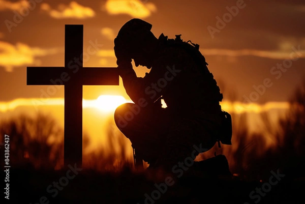 Obraz The silhouette of a soldier kneeling before a battlefield cross, surrounded by the quiet solitude of a setting sun.