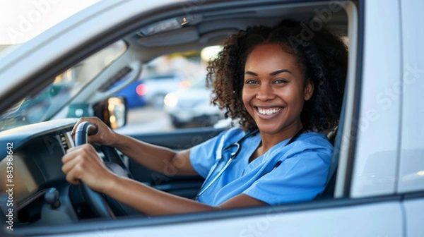 Obraz young african american woman with a joyful expression leans out of a car window, basking in the sunlight. blue medical uniform, a healthcare professional. The background shows a parking 