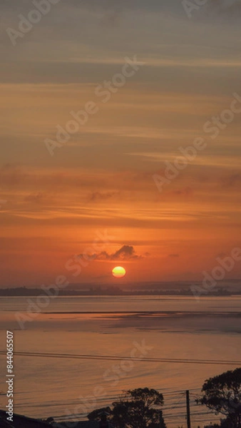 Fototapeta A burning sun rises and peers across an ocean bay through a muted and misty sky.