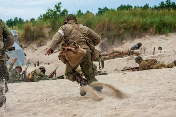 Fototapeta WWII  Historical reconstruction. An American medic during a battle on the beach. View from the back.