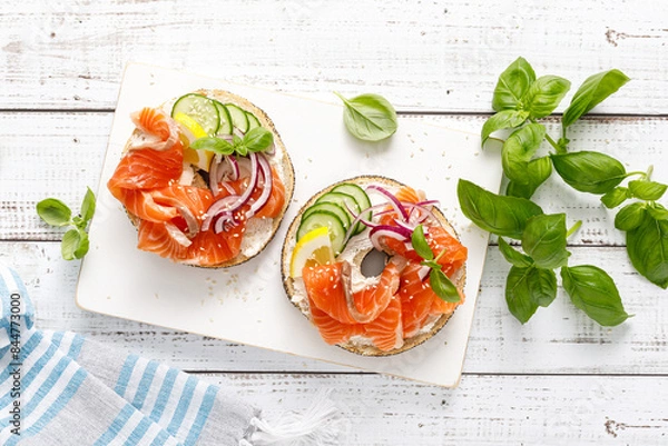 Obraz Salmon sandwiches with bagel, salted fish, fresh cucmber, onion and basil on white background, top view. Healthy breakfast with salmon toasts