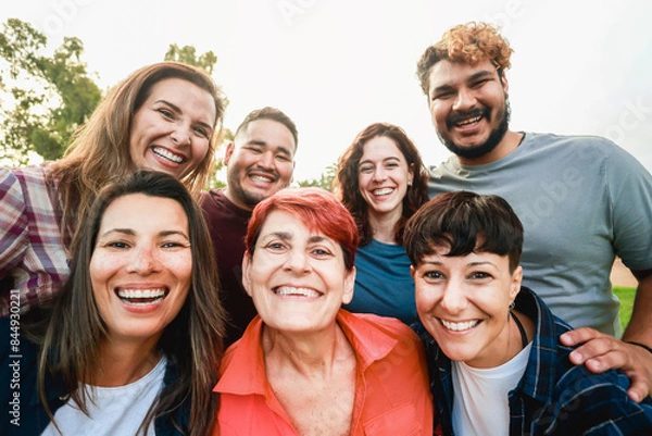 Fototapeta Multiracial friends with different age and ethnicity having fun taking self portrait at park city. Pov of group of people smiling on mobile phone camera