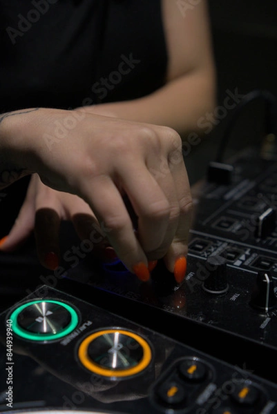 Obraz Close-up photo of a female DJ's hand adjusting controls on a professional audio mixer, showcasing vibrant nail art and high-tech equipment.