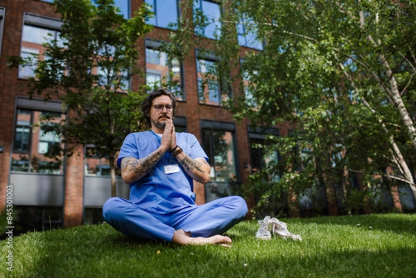 Fototapeta Doctor sitting on grass, meditating and relaxing, winding down from busy workday in hospital. Mental health and life balance for a healthcare worker.