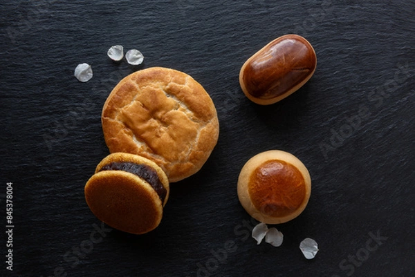 Fototapeta Traditional Japanese sweets, Ume (apricot) flower petals and Japanese green tea in a beauty minimalist aesthetic arrangement on black granite board background. Japan.